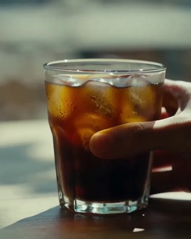 A hand holding an iced coffee on a café table in dappled light.