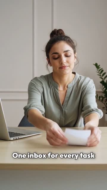 Woman in a green shirt with her hair in a bun, at a desk against a pale wall.