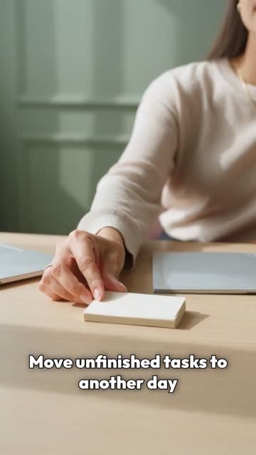 Woman with long brown hair and a pale sweater at a wooden desk against a green wall.